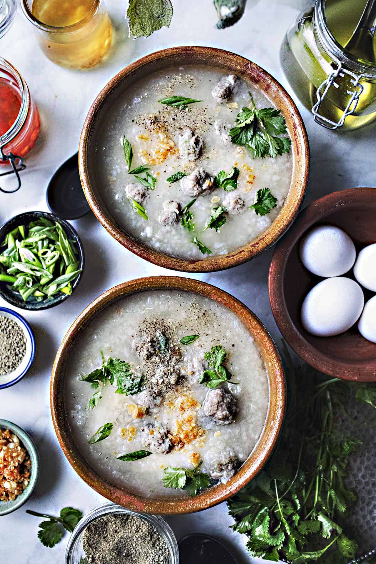 2 bowls of Thai jok soup with garnishes on a table. 