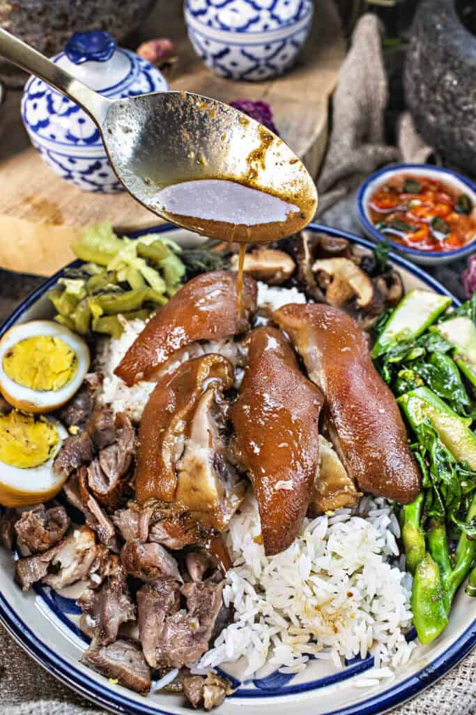 A spoon driping dressing on Khao Ka Moo On a plate.