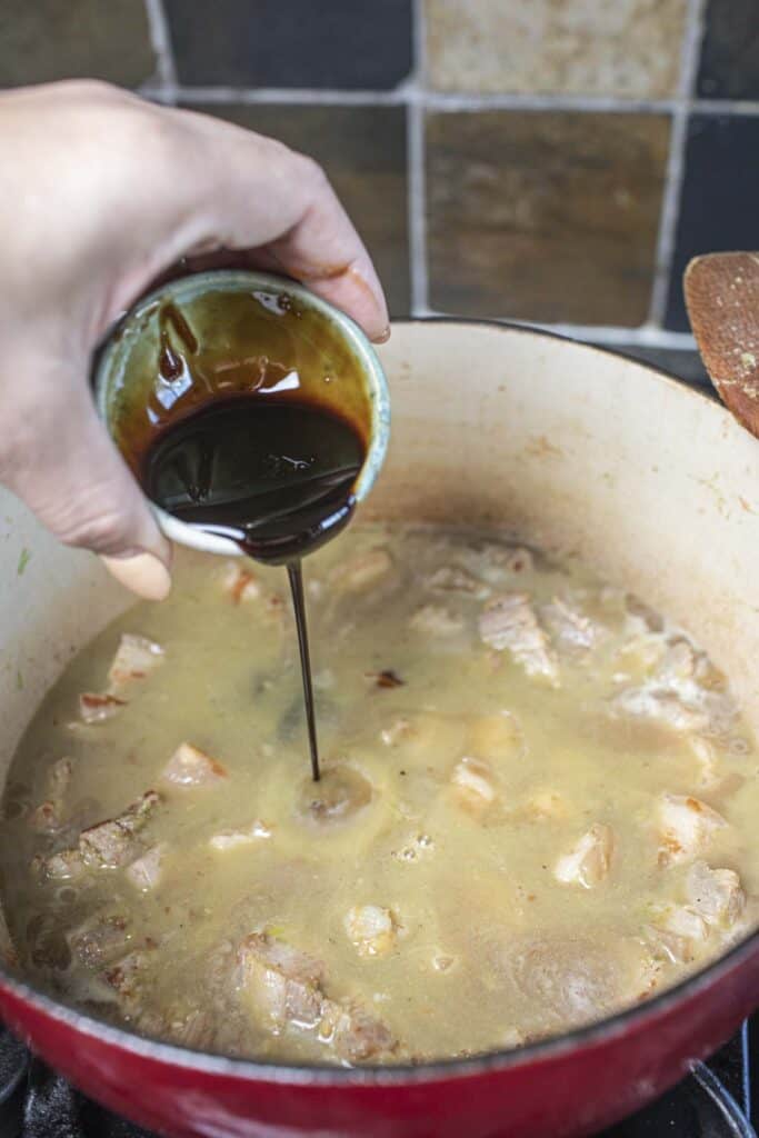Sauce pouring into a stew in a dutch oven.