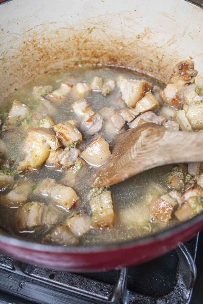 a wooden spoon in a stew in a dutch oven.