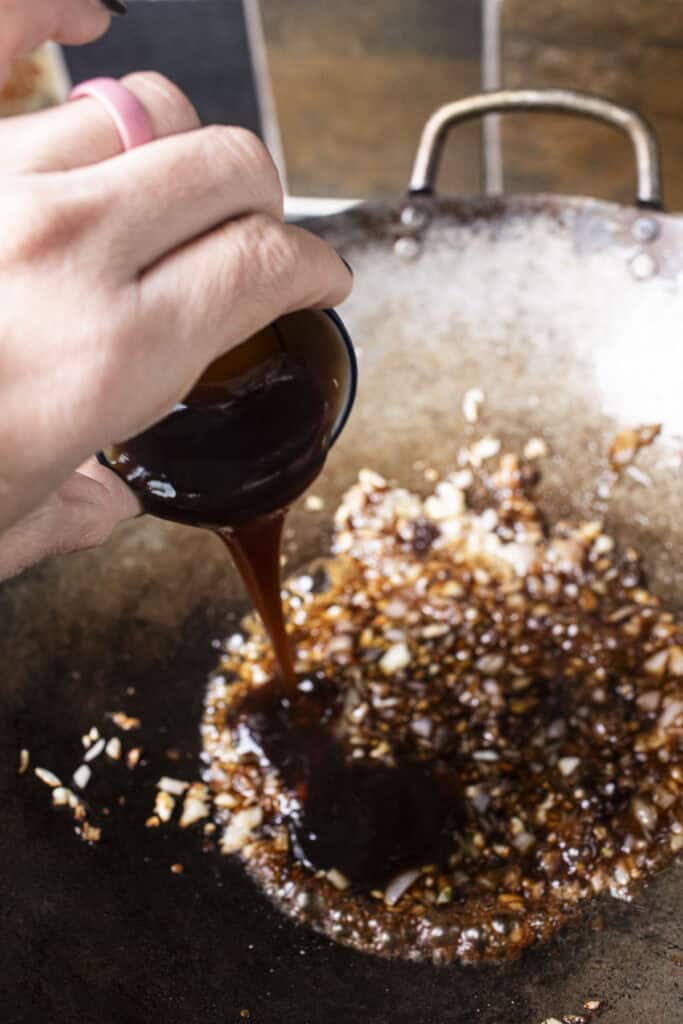 Dark sauce is poured over Kua mee sauce in a wok.