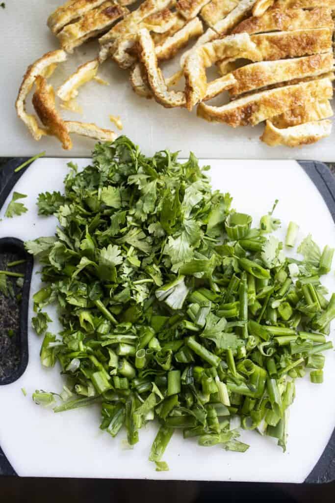Thinly sliced omelet and chopped cilantro and green onion on a cutting board. 