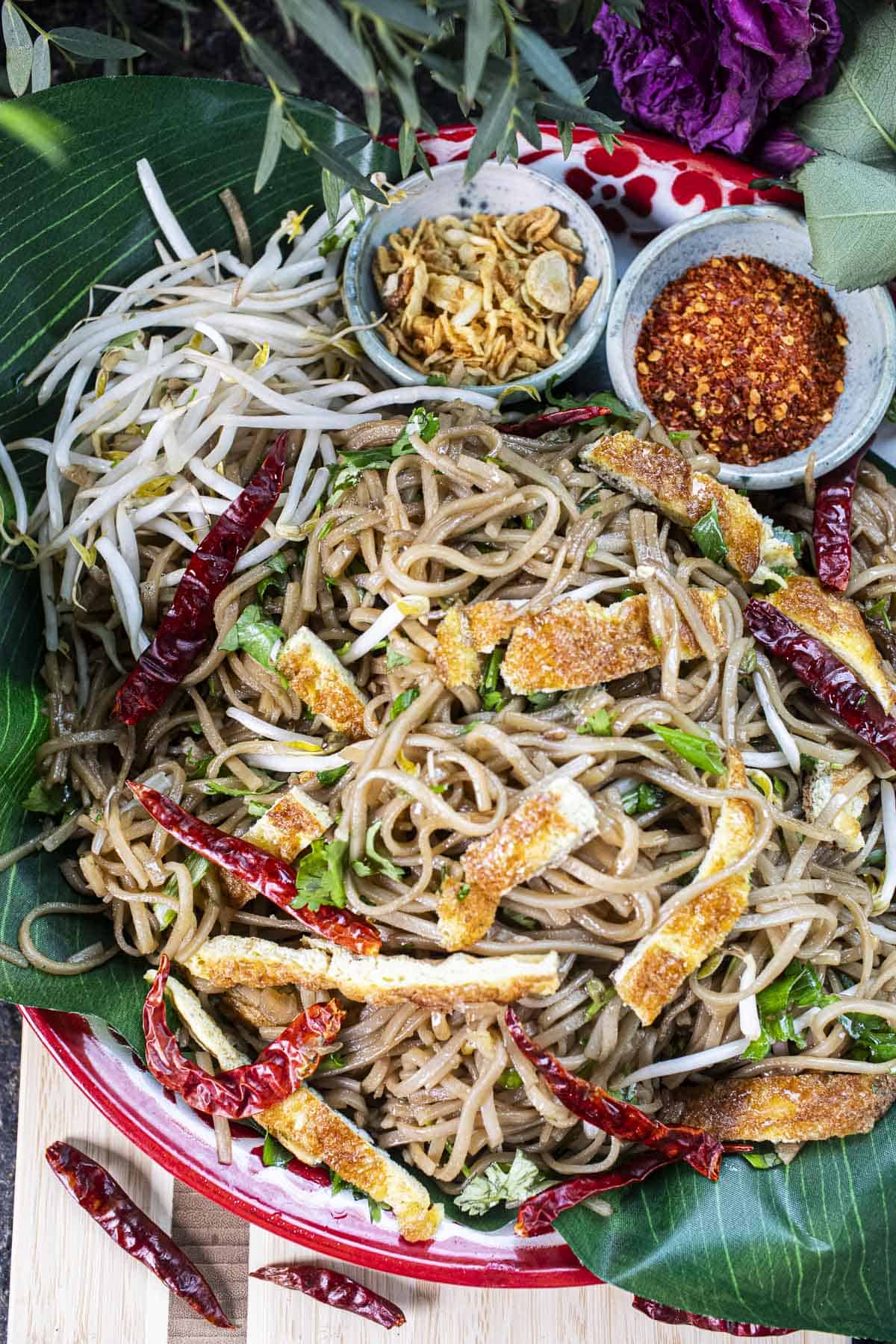 Kua Mee stir-fried lao noodles on a tray with chili and garlic garnishes.