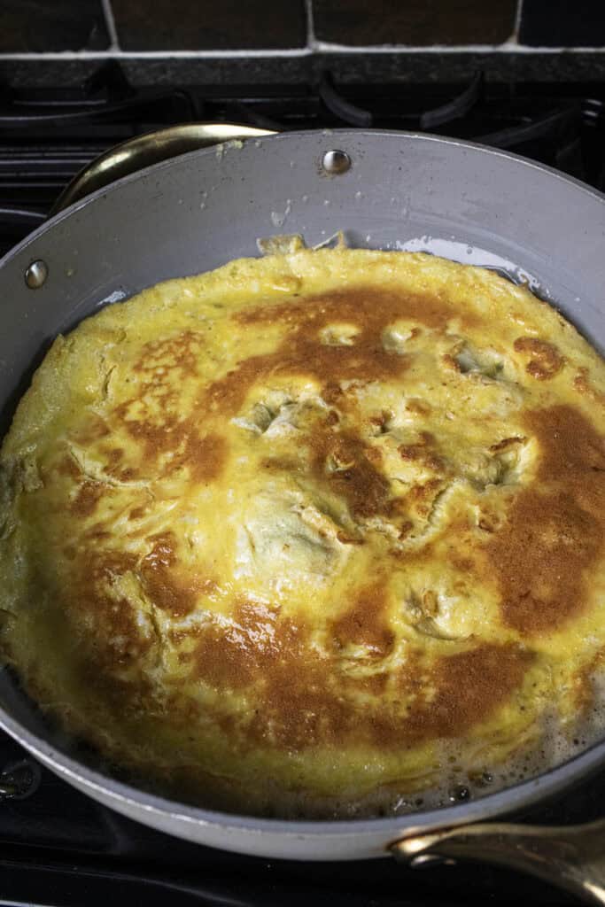 Flat round omelet frying in a large pan.