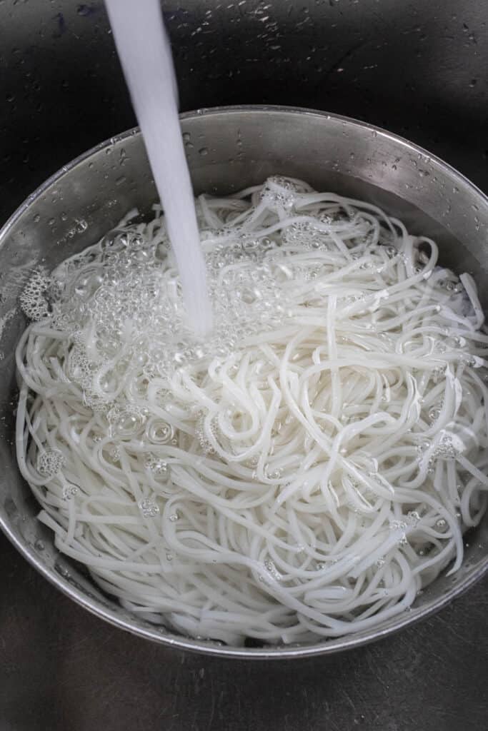 Running water over noodles in a bowl in the sink.