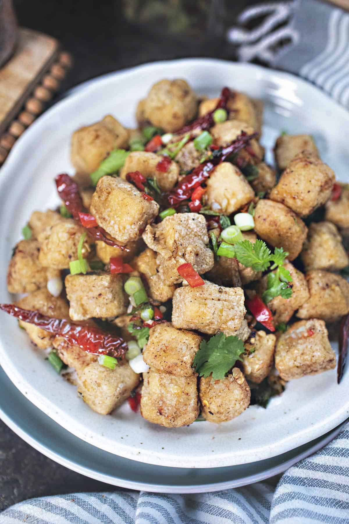 Salt and pepper tofu on a table with garnishes.