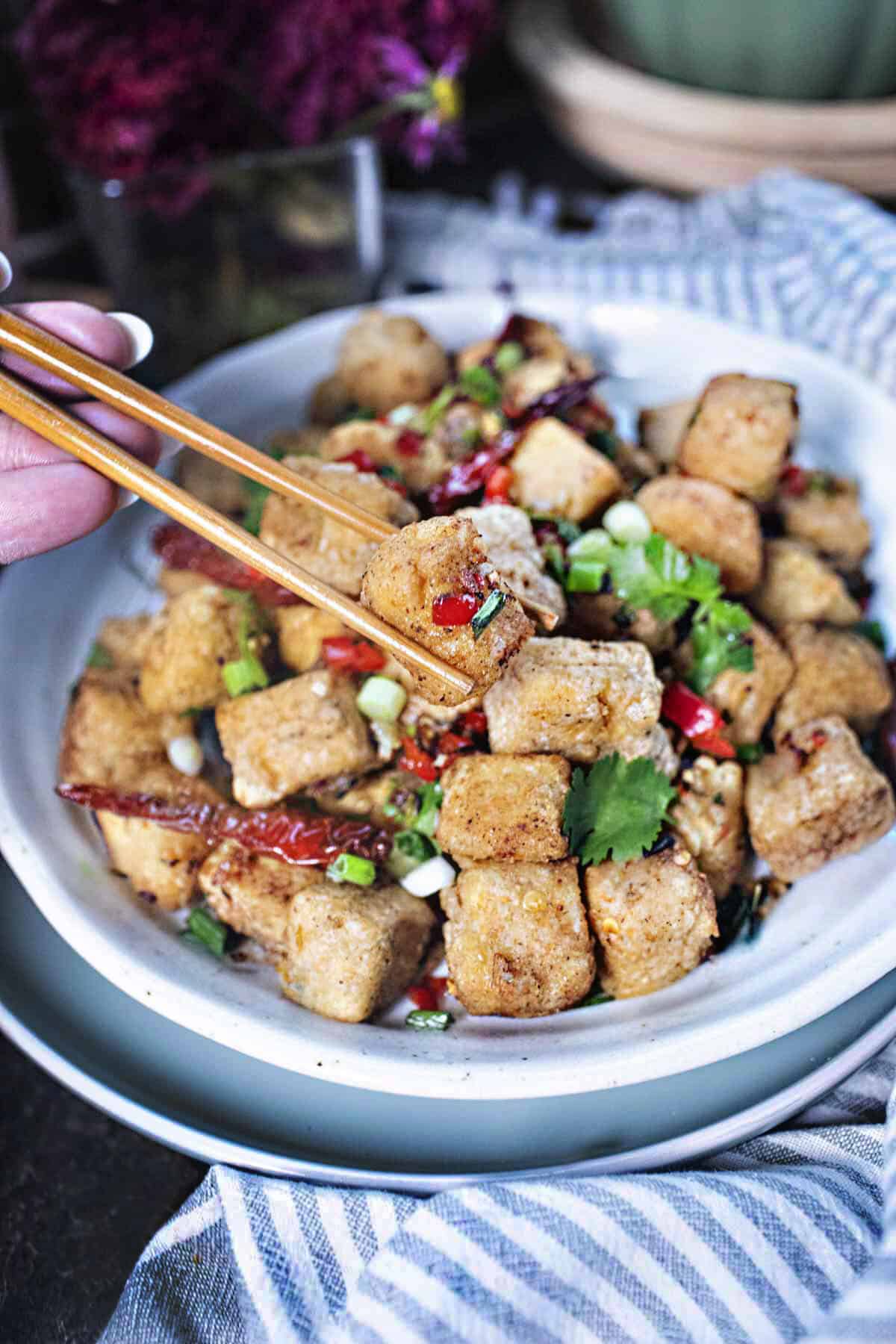 Chop sticks lifting salt n pepper tofu from a plate. 