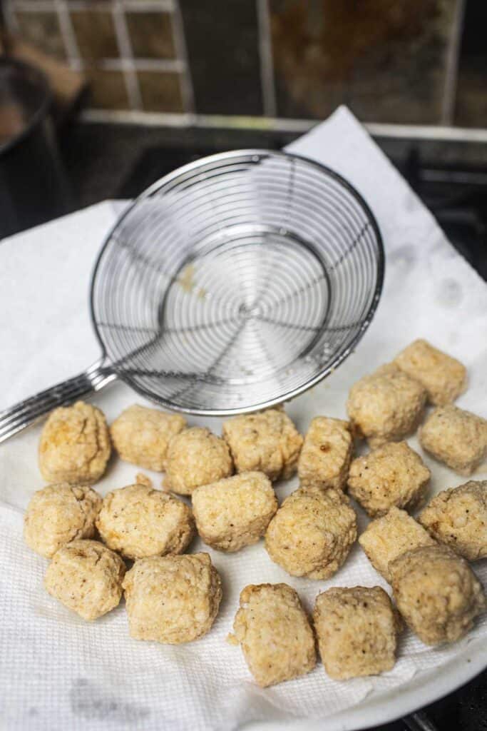 Fried tofu cubes on a paper towel-lined plate. 