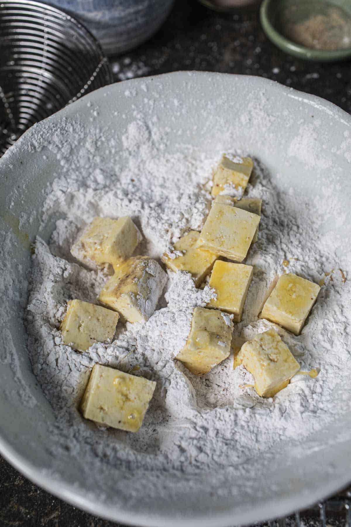 Egg washed tofu cubes in flour in a bowl. 