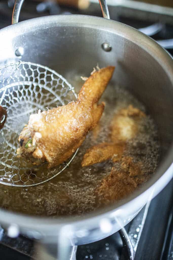 Wire mesh strainer lifting fried wings from pot of oil.