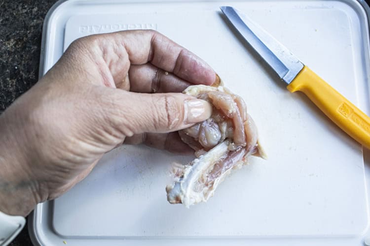 Deboning chicken wing on a cutting b board with a small knife. 
