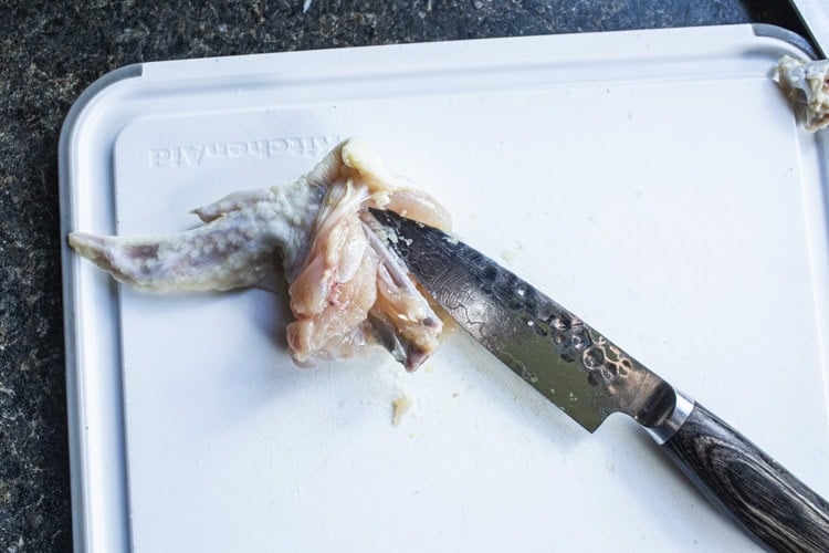 Deboning chicken wing on a cutting b board with a small knife. 
