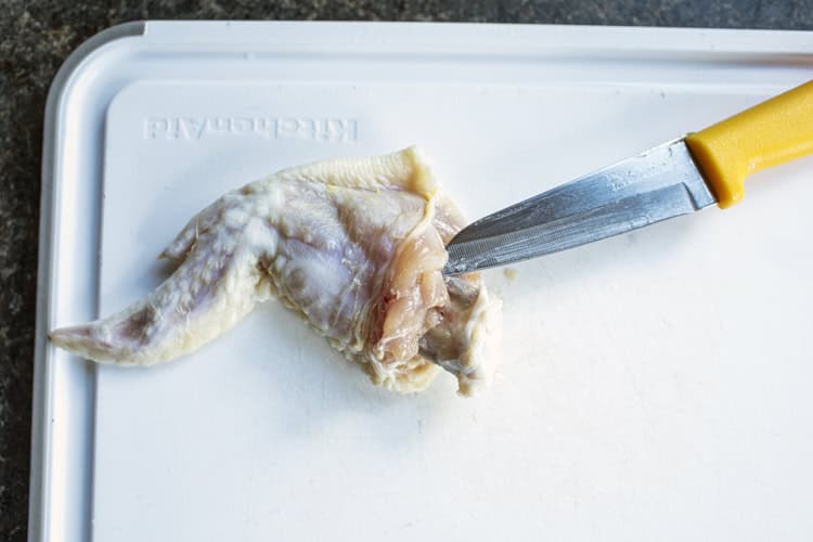 Deboning chicken wing on a cutting b board with a small knife. 