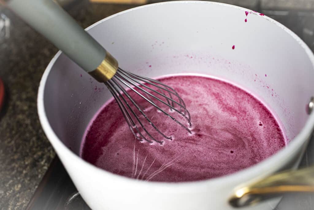 A whisk in a pan with dragon fruit puree.