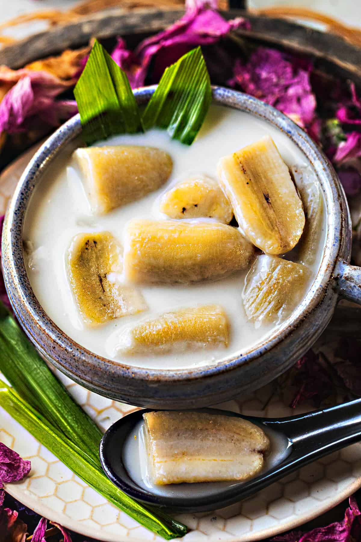 thai banana dessert in a bowl surrounded by pink flower pedals.