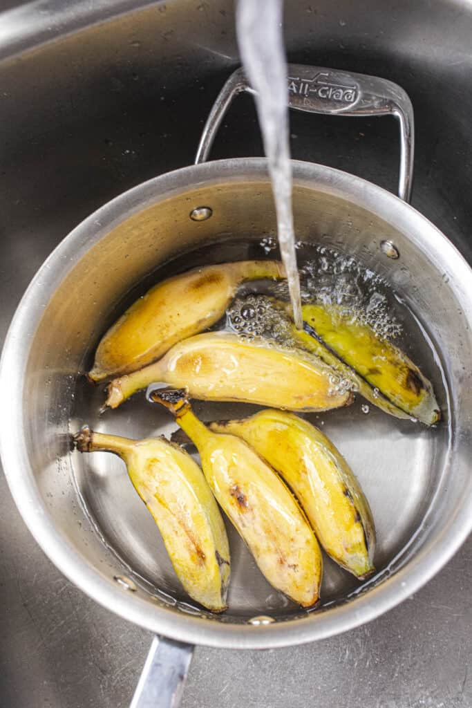 Banana with peels in a pot of running water. 