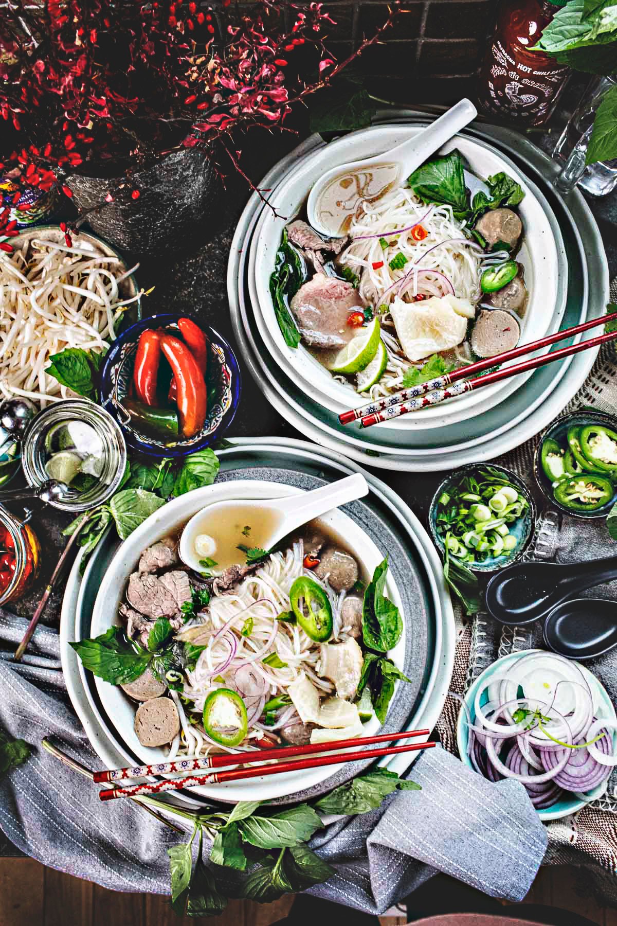 Beef pho noodle soup in 2 bowls with garnishes on the side.