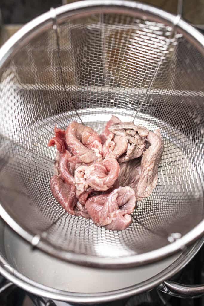 Sliced beef in a wire mesh strainer.