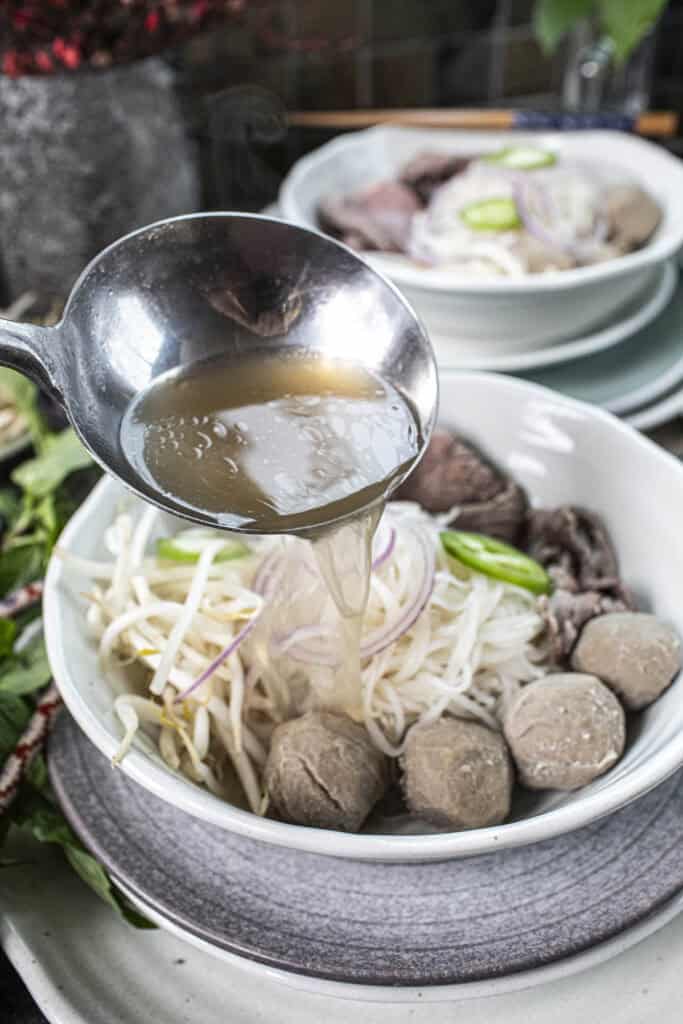 Broth pouring into a bowl of pho. 