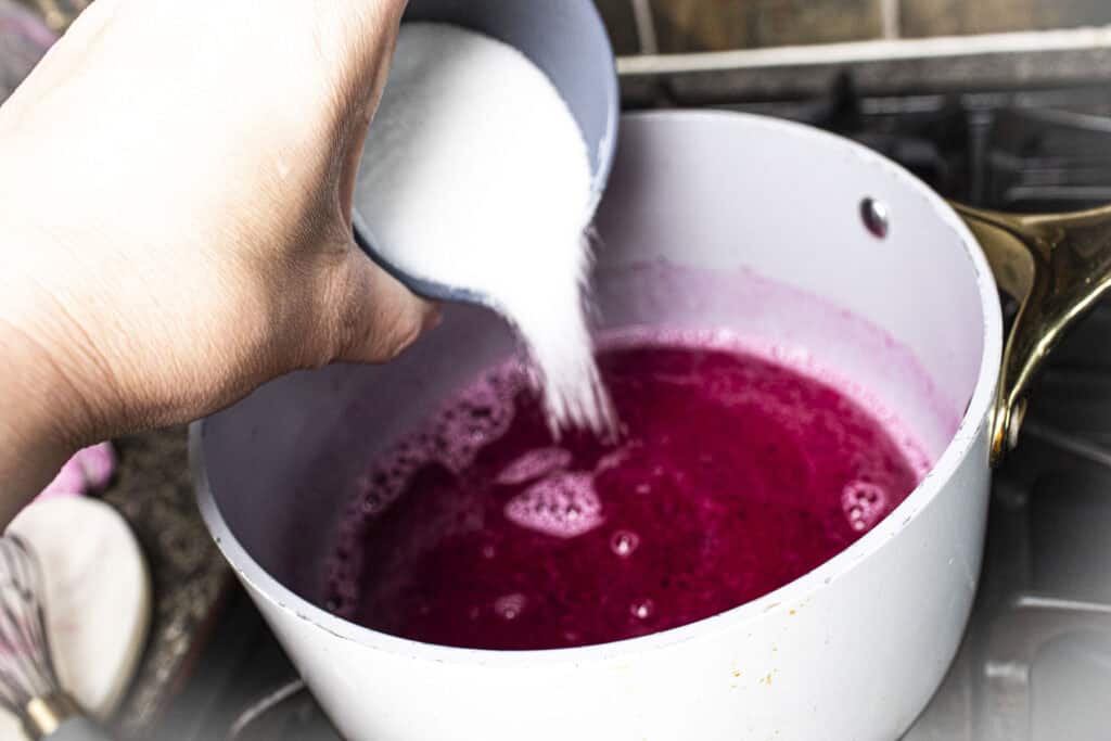 Sugar pouring into a pan with dragon fruit puree.