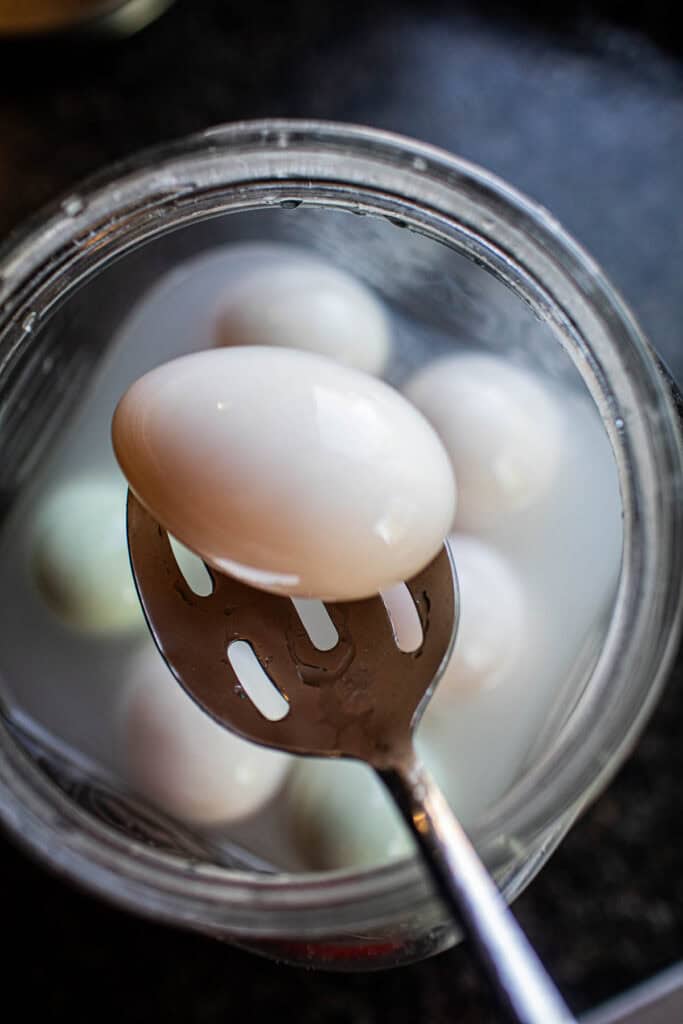A spoon lifted salted duck eggs from a jar. 