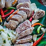 Sliced Nam sausage on a platter with rice and Thai chilis.