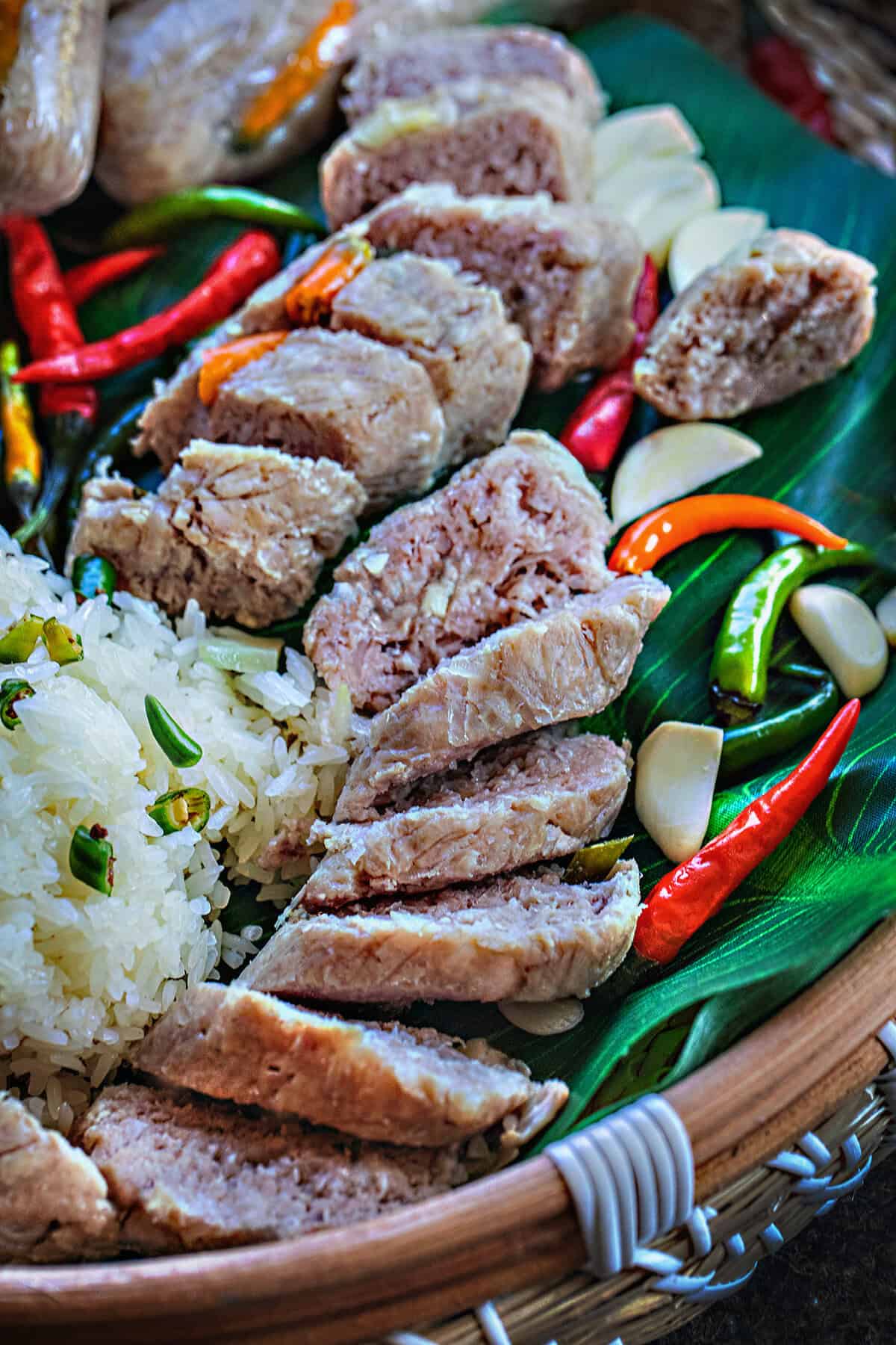 Sliced Nam sour sausage on a platter with rice and Thai chilis. 