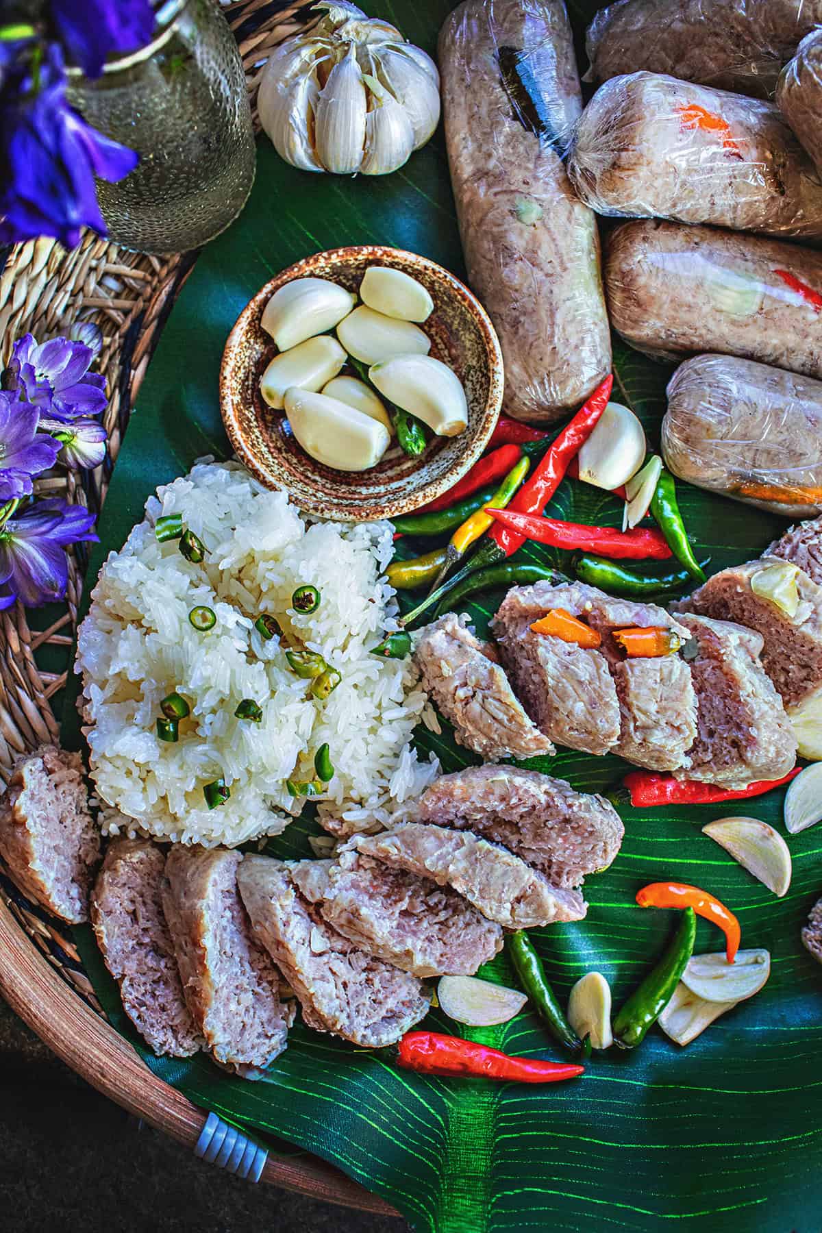 Sliced Nam sausage on a platter with sticky rice and Thai chilis.