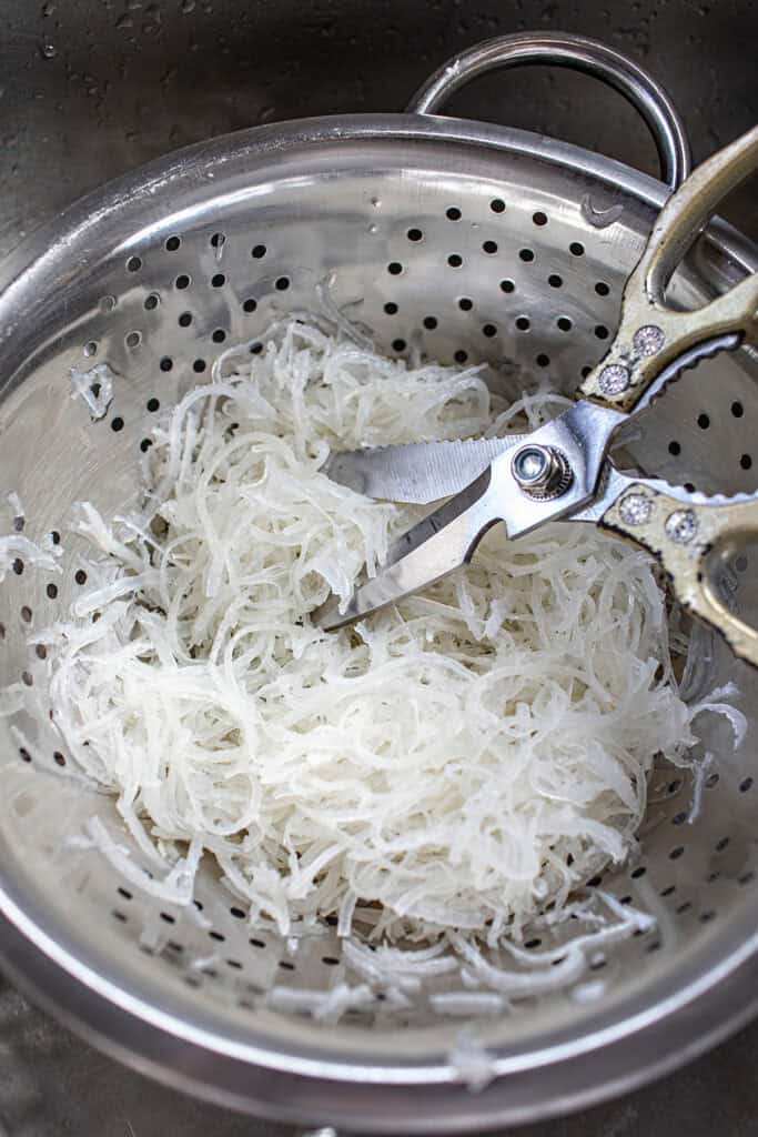 a scissor-cutting pork skin in a colander. 