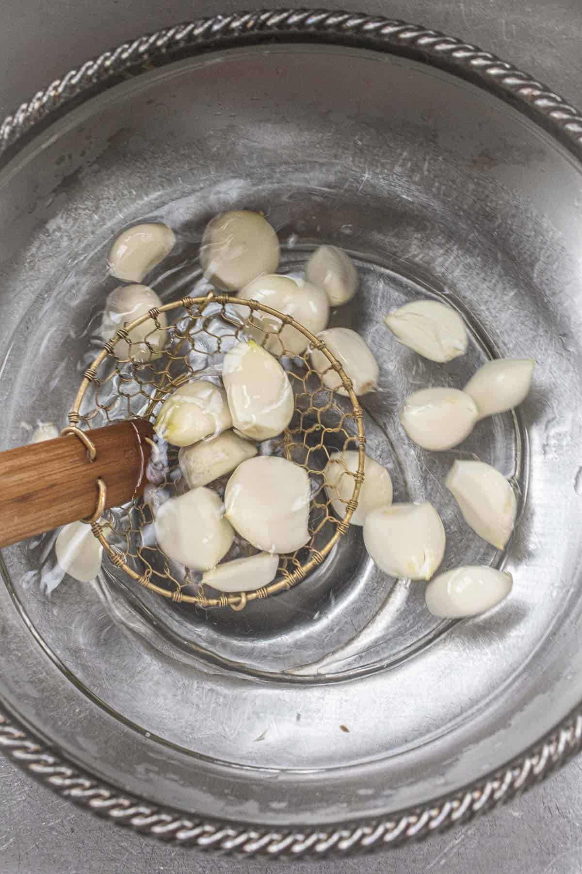 Wiremess strainer lifting Garlic cloves from a glass bowl. 