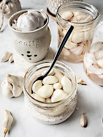 thai pickled garlic in a glass jar with a spoon and other glass jars around it.