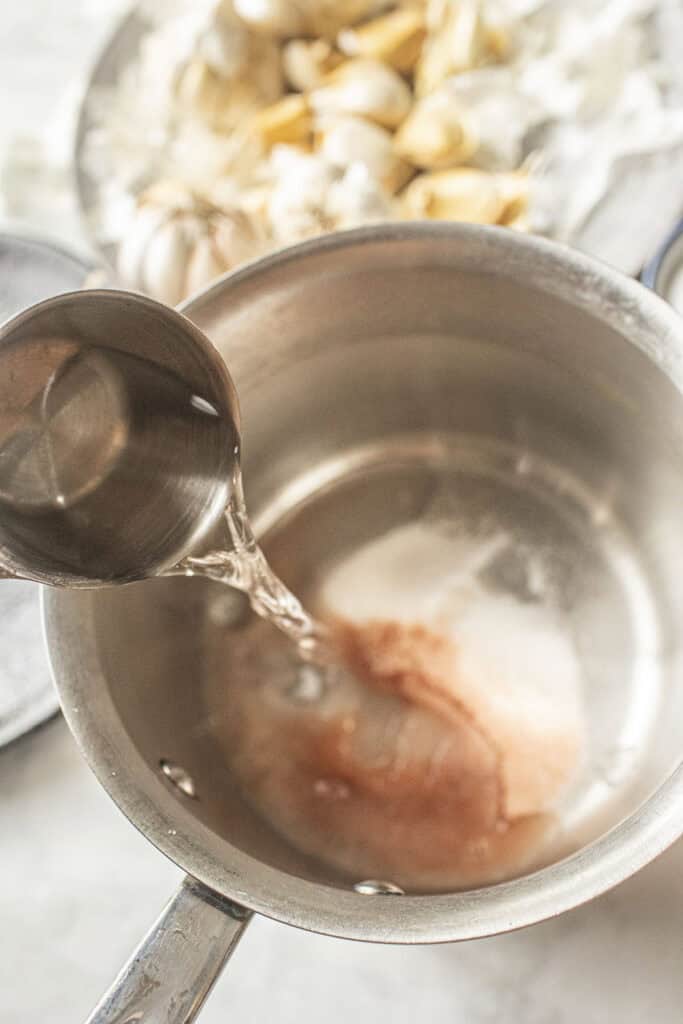 A cup of water pouring into a soup pot with pickling brine.