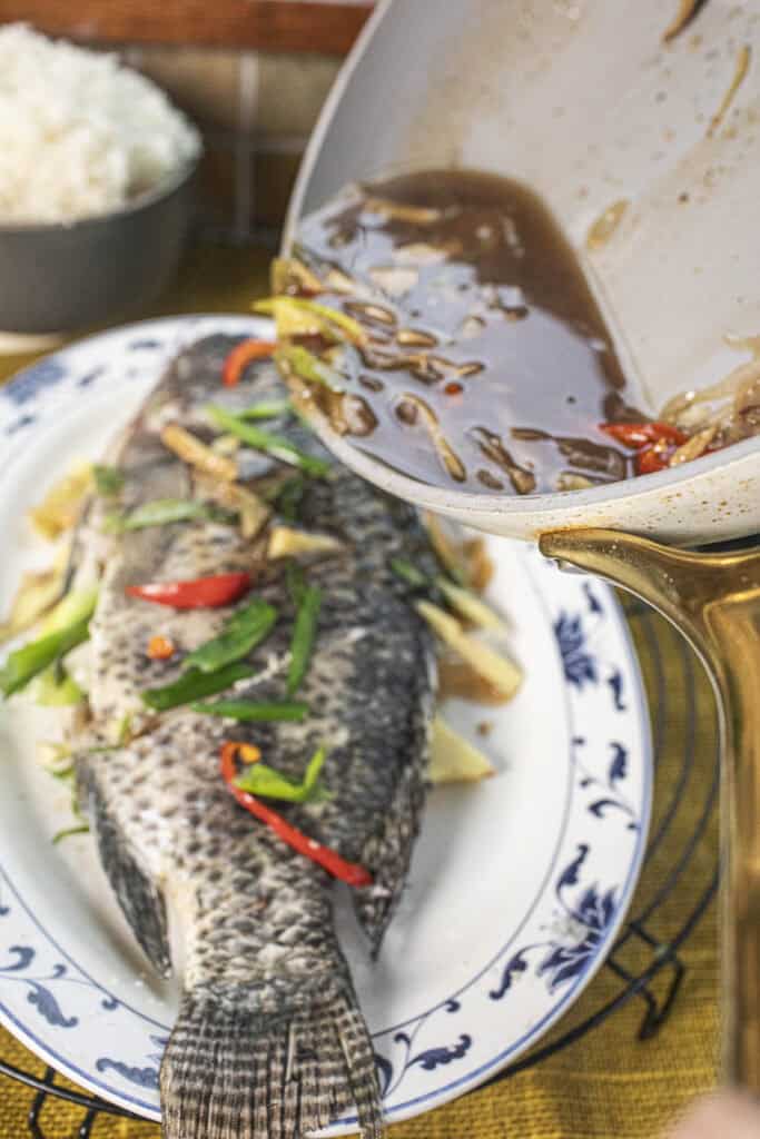 soy sauce mixture pouring ove a whole steamed fish. 