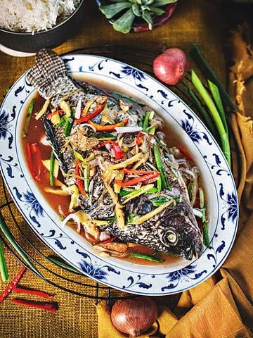 Chinese steamed fish with soy sauce and herbs on a plate.