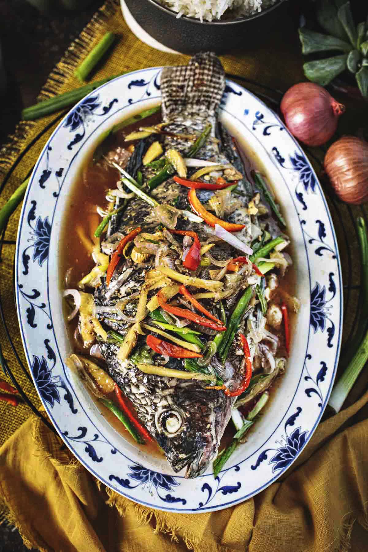 cantonese steamed fish with herbs on top on a platter.