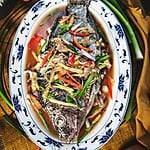 Steamed fish with soy sauce and aromatics on top of the fish on a platter.