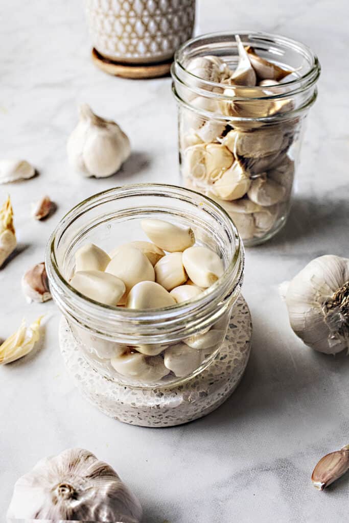 Garlic cloves in 2 glass jars on the table.  