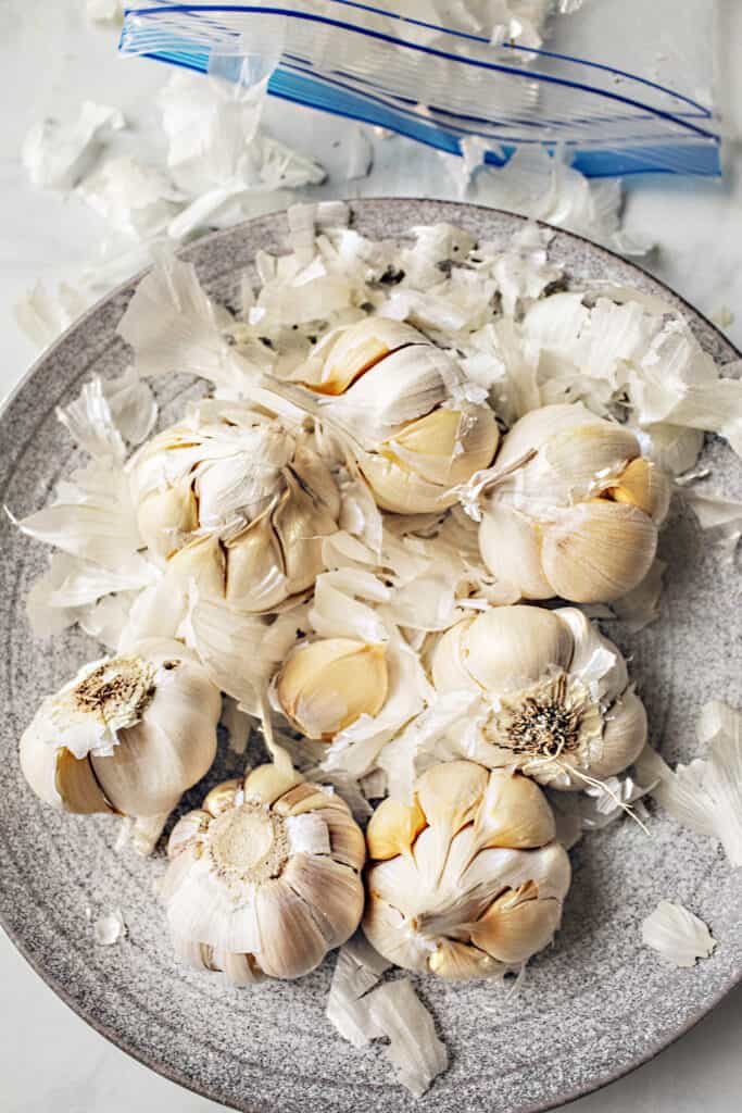 Garlic heads and cloves with peels around on a plate. 
