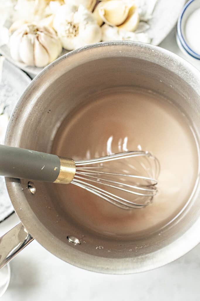 A whisk in a soup pot with pickling brine.