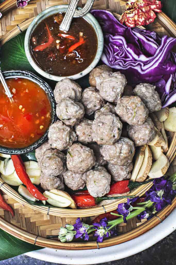 Thai luk chin meatballs on skewers on a tray with dipping sauce. 