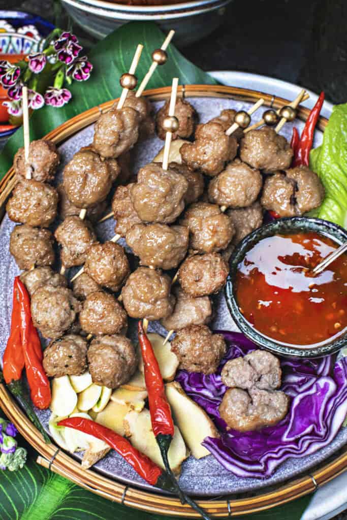 Thai pork meatballs on skewers on a tray with dipping sauce. 