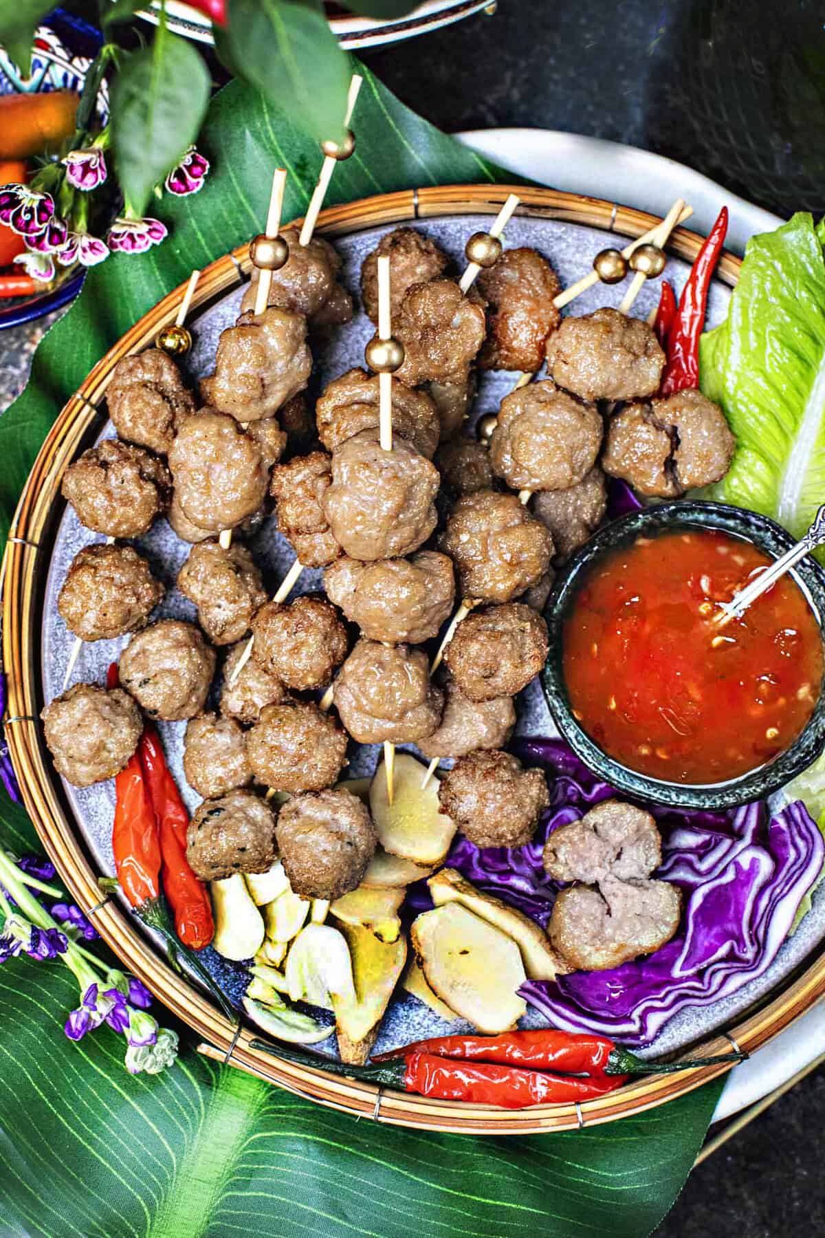 thai pork meatballs luk chin in skewers on a platter.
