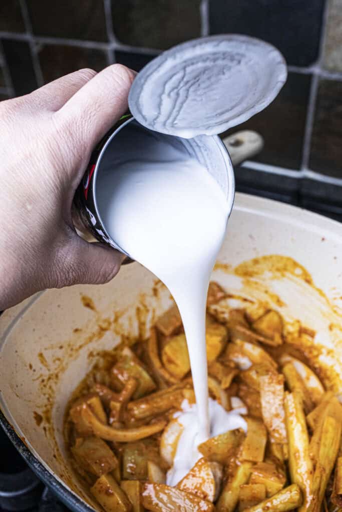 Coconut milk from a can poured into a pot with curry.