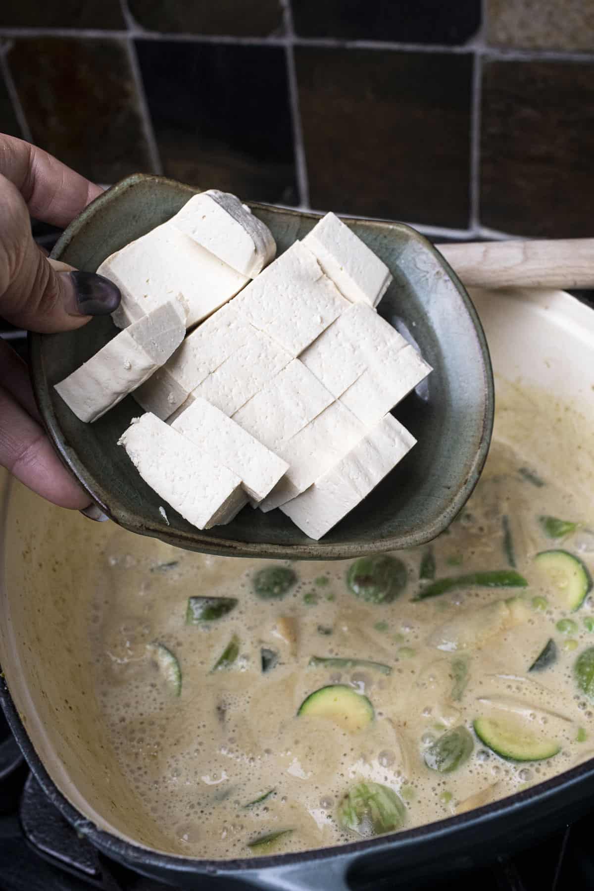Addin tofu slices into a pot of green curry.