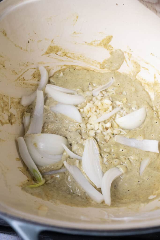 Garlic and onion in green curry paste in a pot.