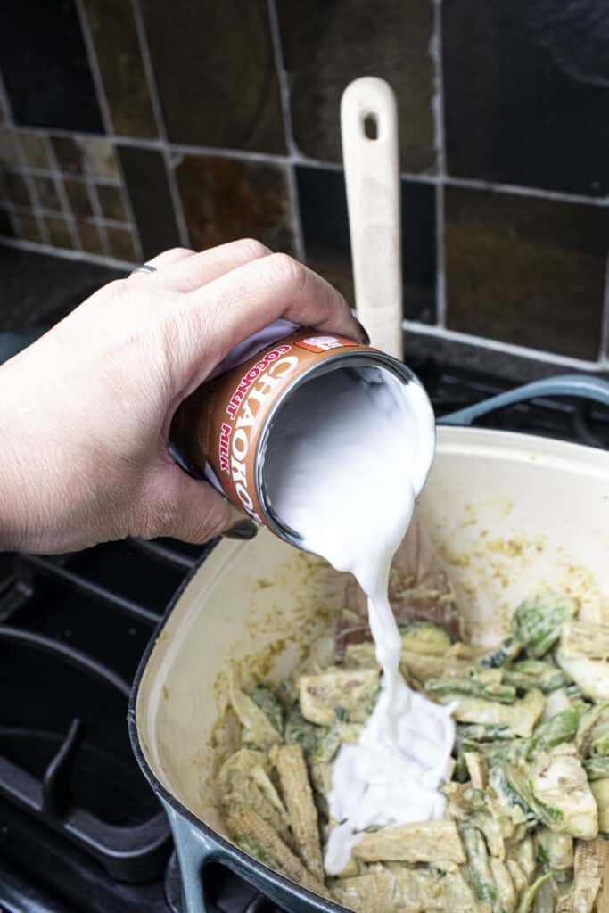 coconut milk from a can pouring into a pot of vegetarian curry. 