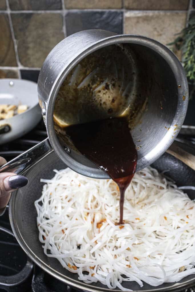 Sauce is poured into Pad Thai noodles in a wok.