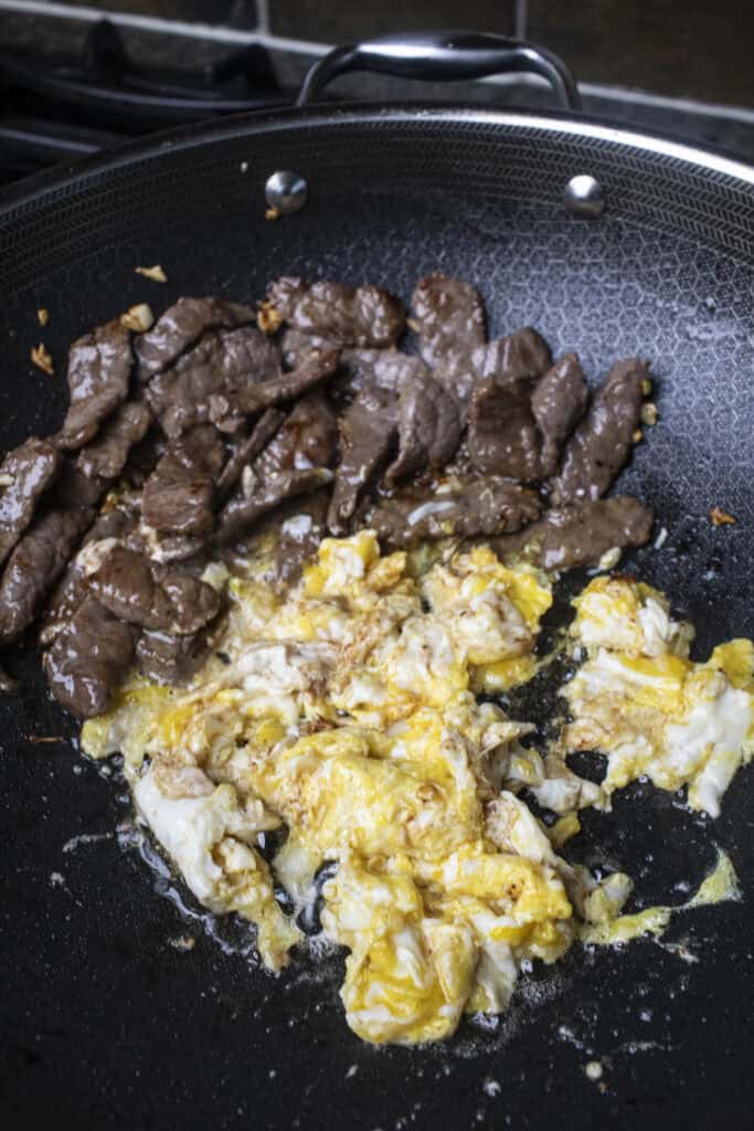 Sliced beef and scrambled eggs for pad see you stir fry in a wok.