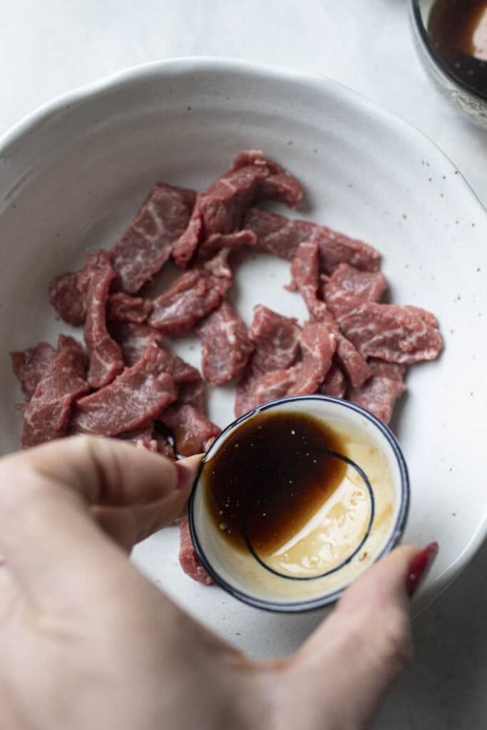 Pad see ew sauce pouring over sliced beef. 