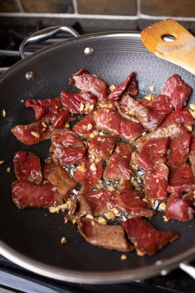 Sliced pork with minced garlic is being cooked in a wok. 